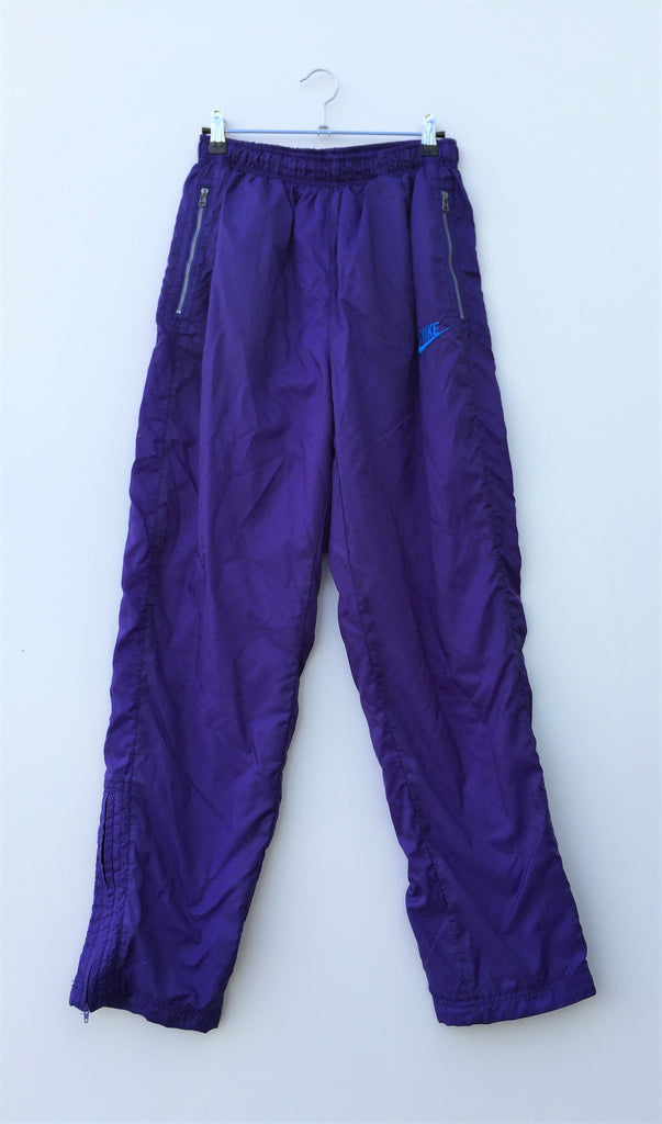 Acheter un pantalon de survêtement "grande marque" en Auvergne Rhône-Alpes. Pantalon de survêtement violet vintage années 90. 2 poches zippées. Doublure blanche à l’intérieur. 2 zips aux chevilles. Ceinture élastiquée à la taille. Marque:Nike Taille: 38 Composition: Composition: tissu extérieur: 100% nylon, Doublure: 65% polyester, 35% coton. 